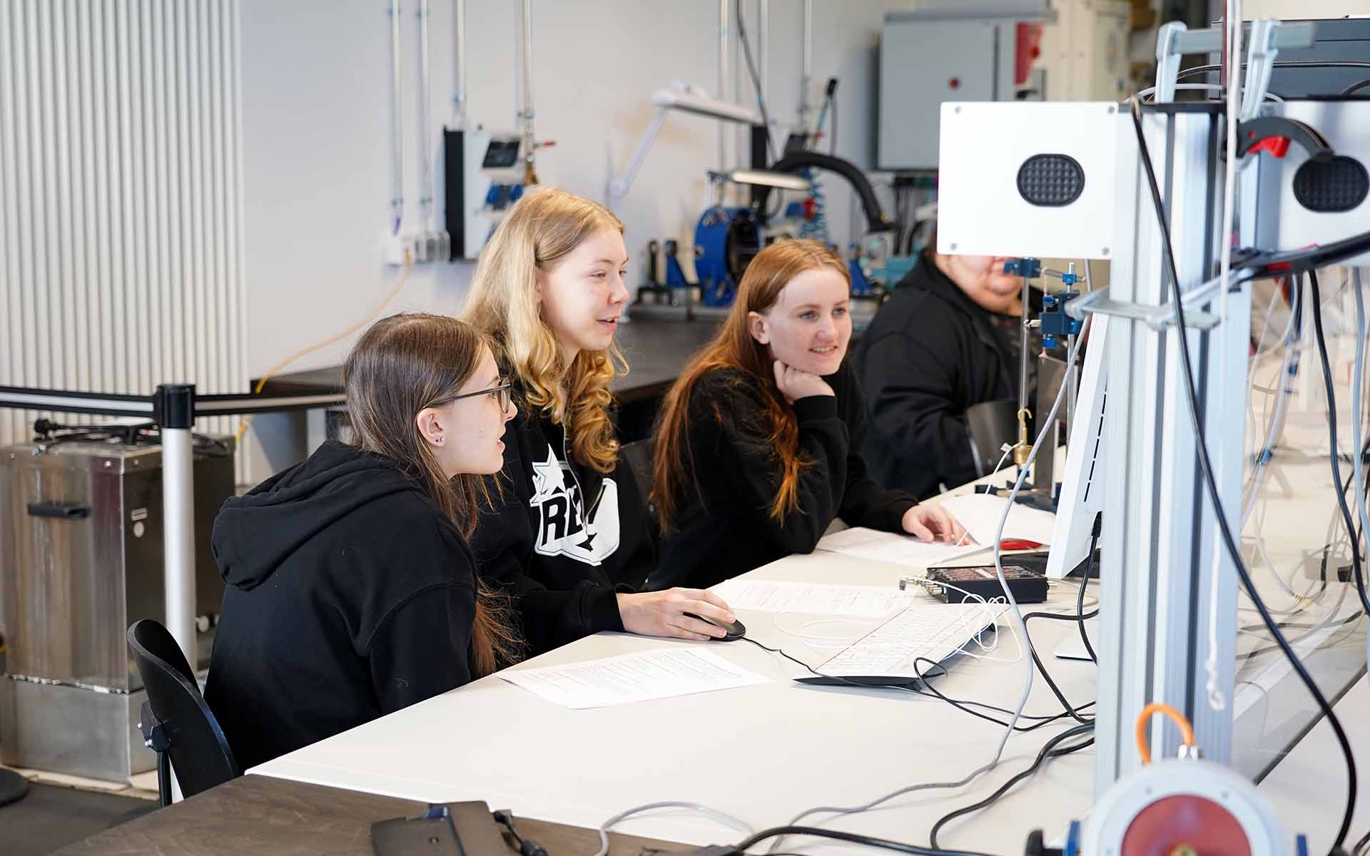 Drei Mädchen sitzen an einem Tisch vor einem Laboraufbau mit Computer