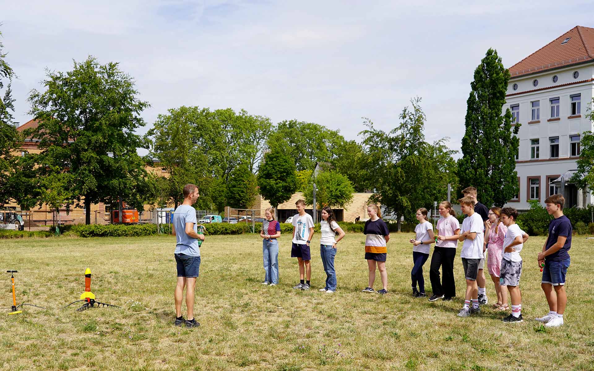 Laboringenieur Sebastian Zeising steht auf der Campuswiese und erklärt den Schülerinnen und Schülern das anstehende Experiment mit der kleinen Rakete, die hinter im steht