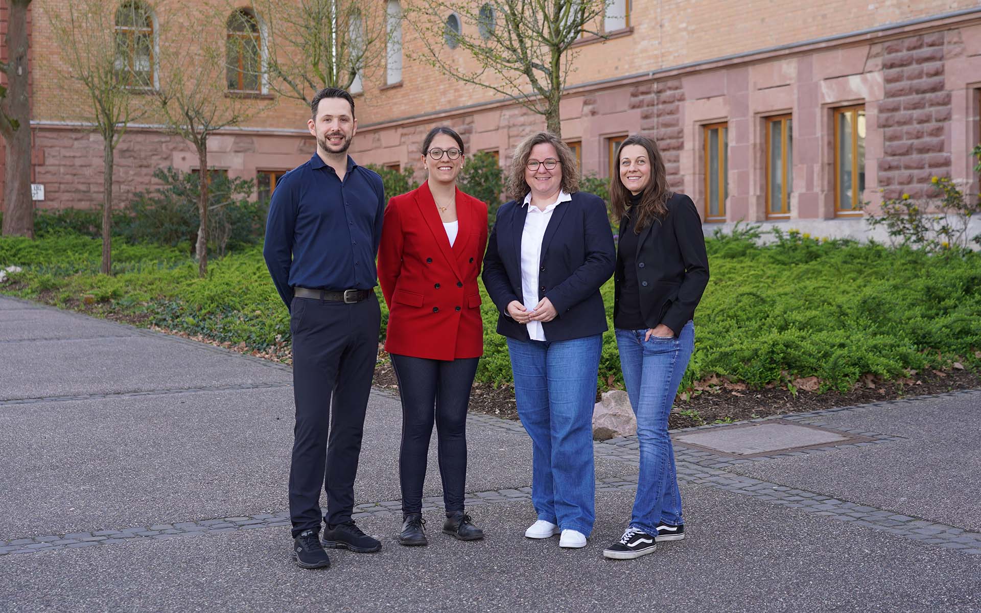 Drei Professorinnen und ein Professor der Fakultät Gesundheitswissenschaften stehen nebeneinander auf dem Campus vor einem Gebäude mit rotbraunen Backsteinen