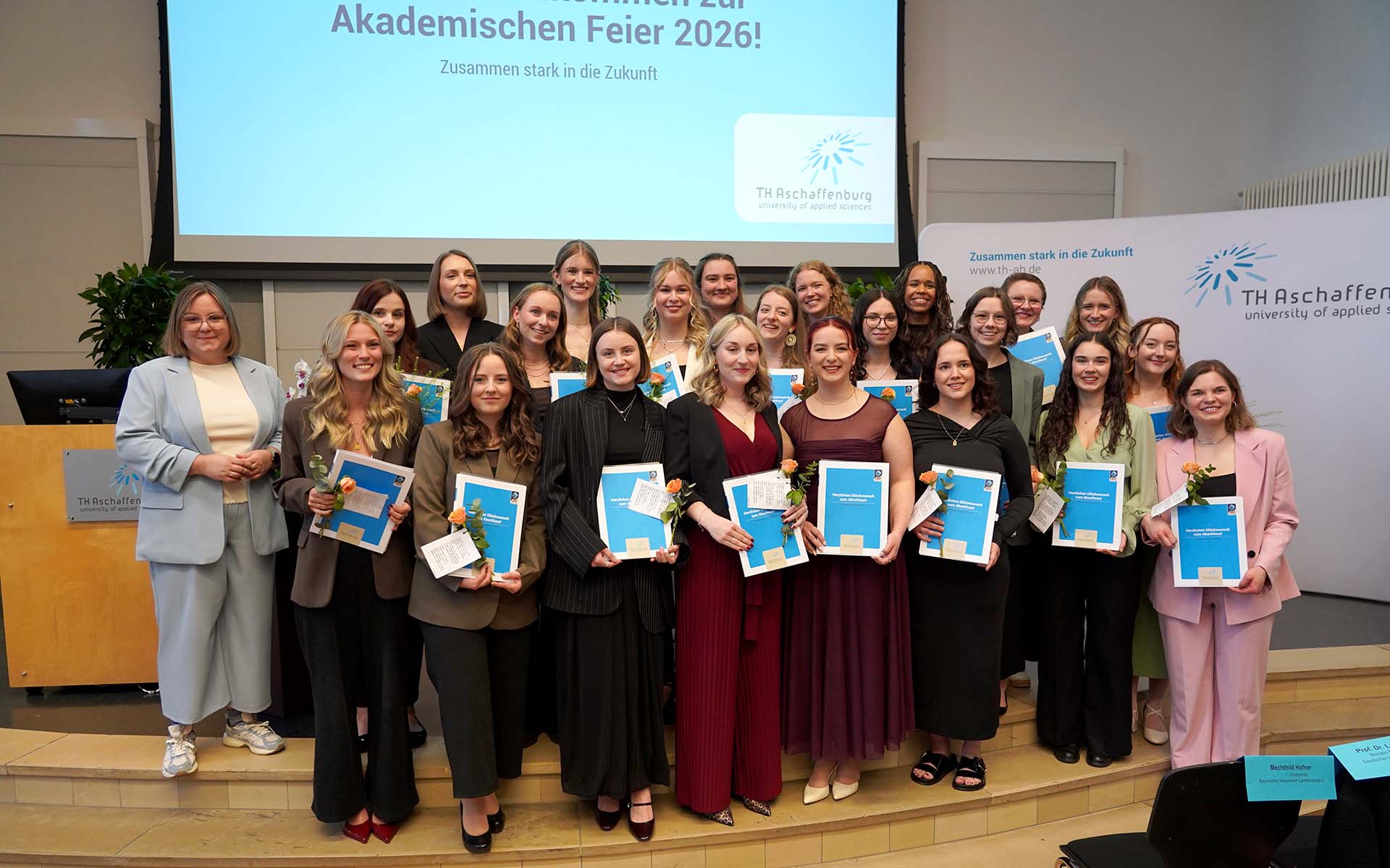 Gruppenbild der 23 Absolventinnen mit Urkunden und je einer Rose in der Hand zusammen mit Dekanin in der Aula