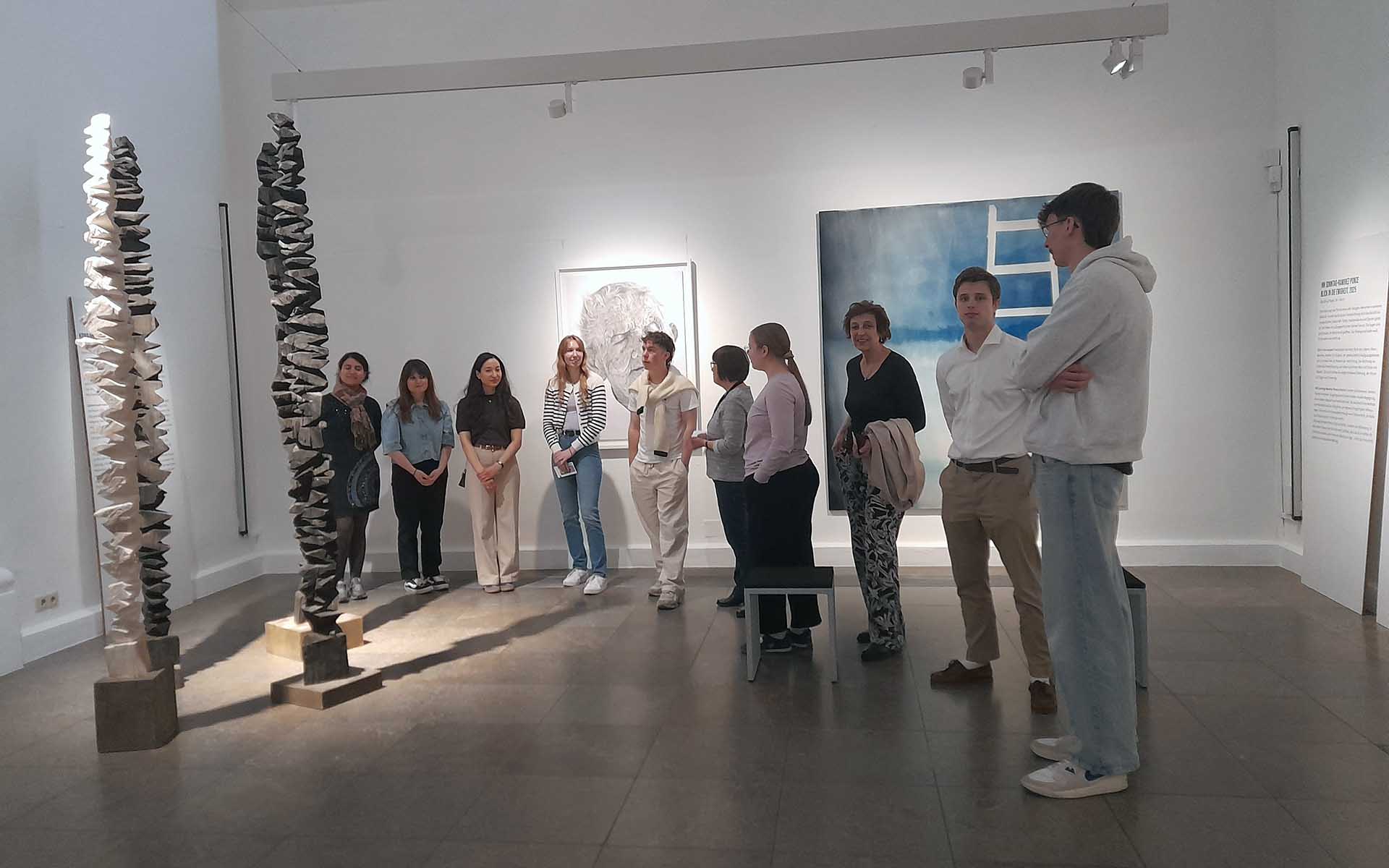 Studierende stehen im Halbkreis mit Präsidentin vor einem Kunstwerk