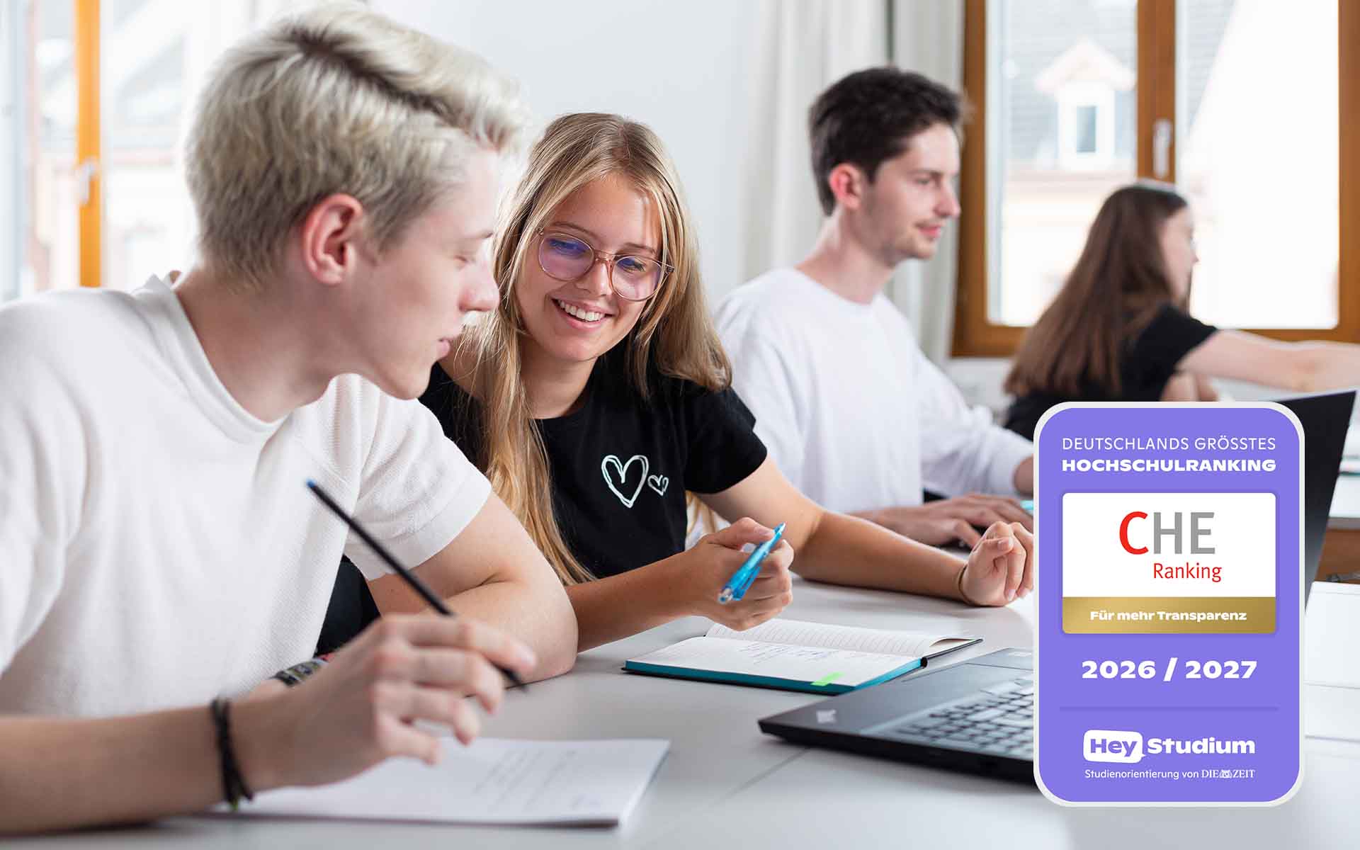 Vier Studierende sitzen vor Laptops an Tischen, Siegel zum Ranking im Vordergrund