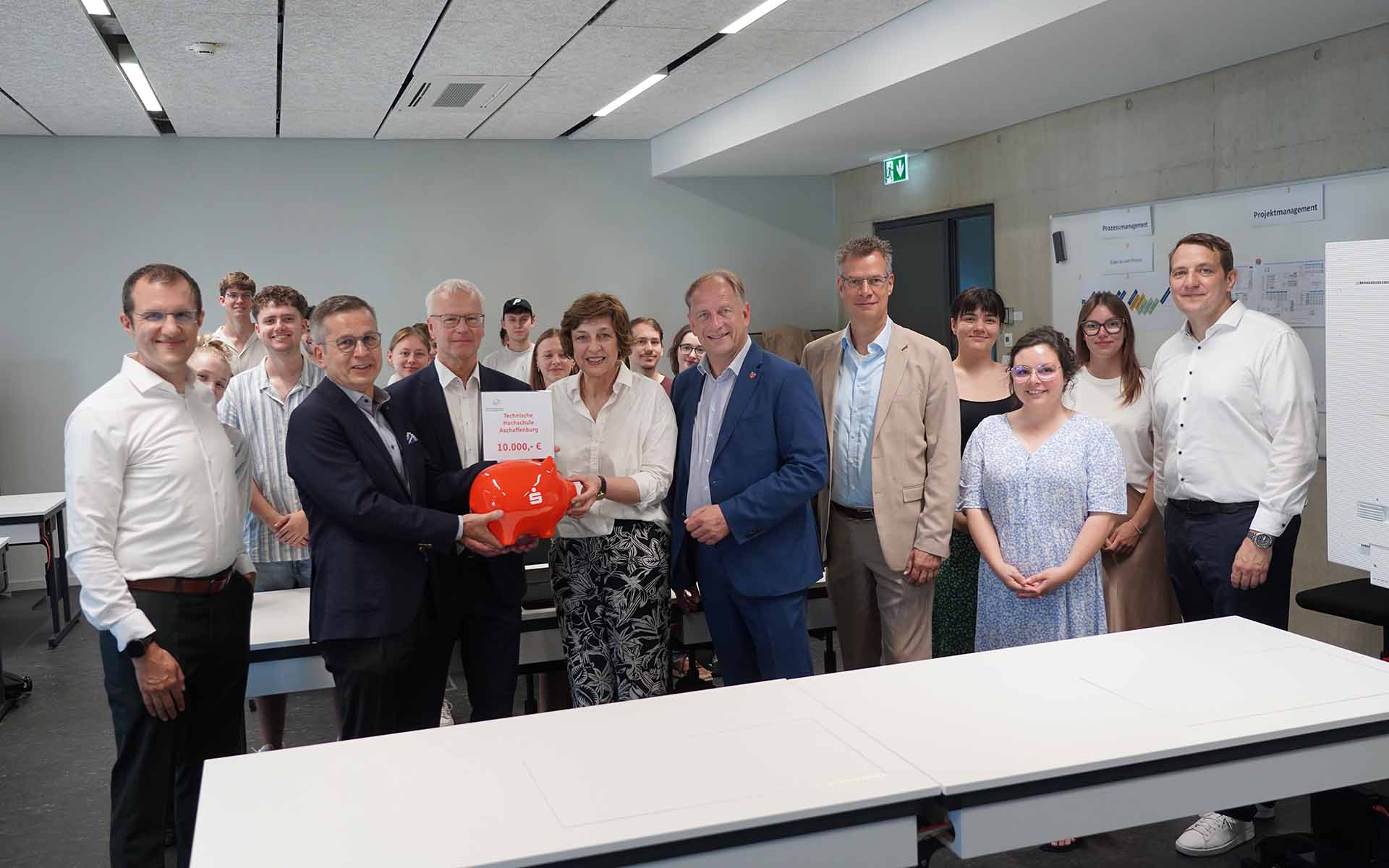 Gruppe von 7 Personen mit Sparschwein und Studierenden dazwischen und dahinter