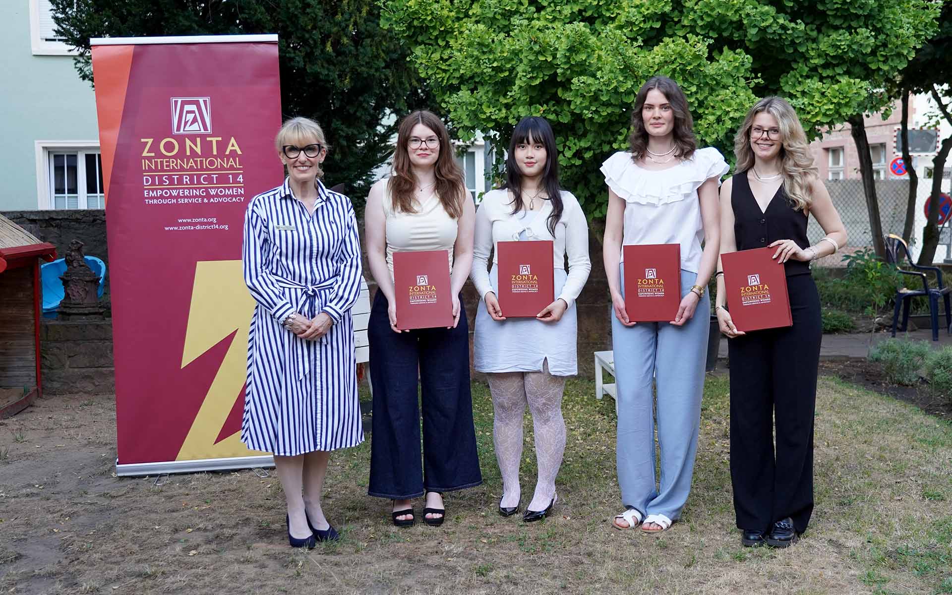 Zonta-Präsidentin mit den vier Preisträgerinnen mit Urkunden in der Hand vor Zonta-Roll-up