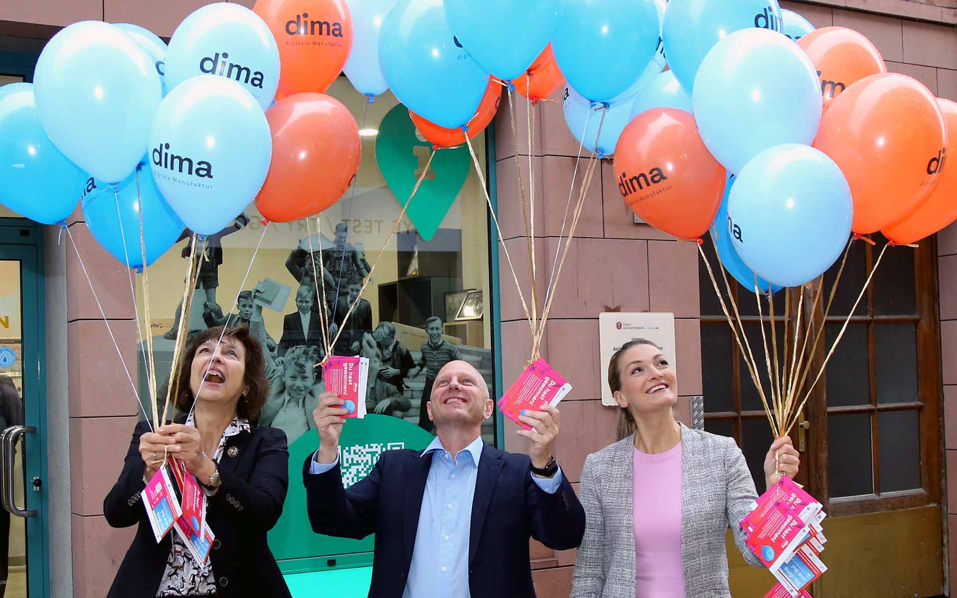 Drei Personen stehen nebeneinander und blicken auf rote und blaue Luftballons, die sie in den Händen halten und an denen Karten hängen