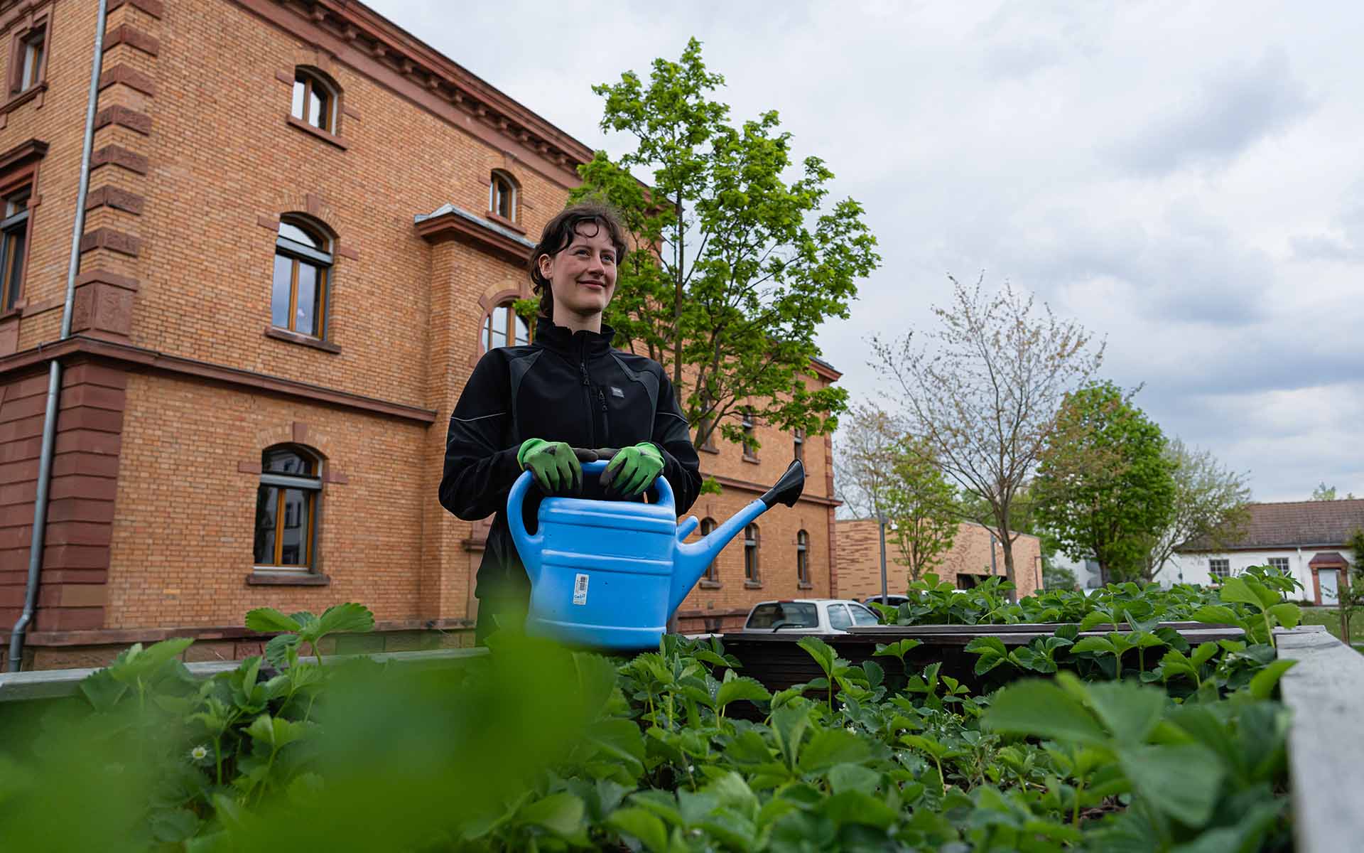 Eine junge Frau, die den Hochschulgarten gießt